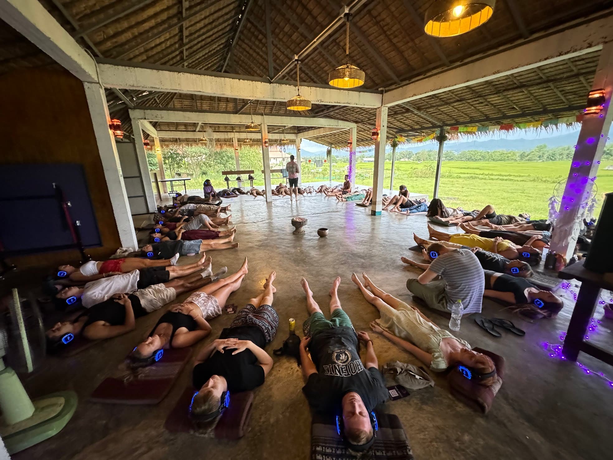 A full room in deep trance, participants lying on the floor with glowing headphones under warm lantern light.